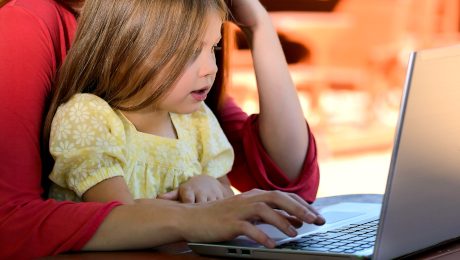 Dziewczynka siedząca na kolanach kobiety przy stole przez laptopem